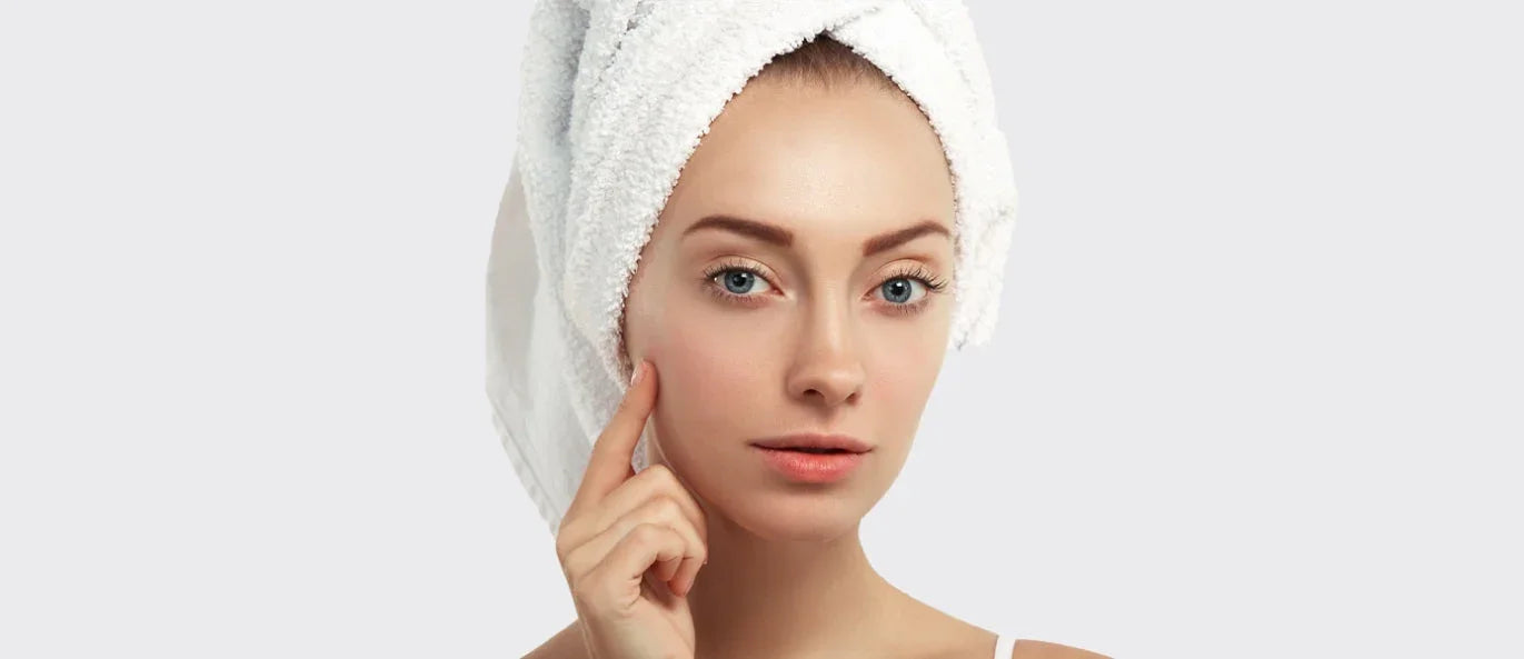 Woman with clean skin and towel wrapped hair touching cheek, skincare concept